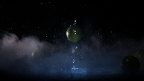 Lime Fruits Falling on Water Surface in Blue Light Spot and Cold Fog Cloud