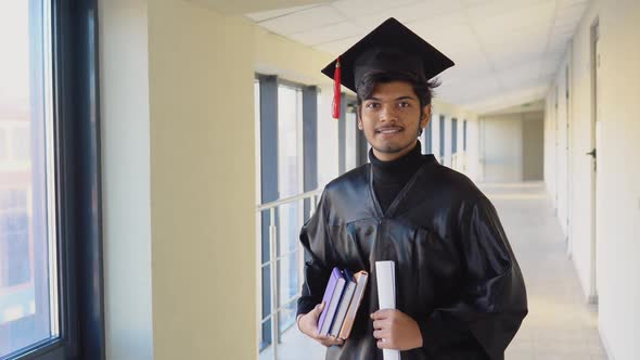 Indian Graduate in Mantle Stands with a Diploma and Books in Her Hands and Smiles