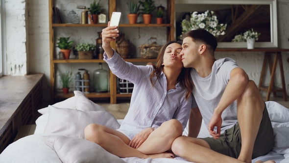 Cheerful Loving Couple Is Taking Selfie with Smartphone Looking at Camera, Posing and Making Funny