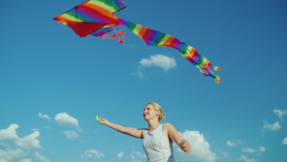 Happy Woman As a Child Plays with an Air Kite on a Background of Pure Blue Sky