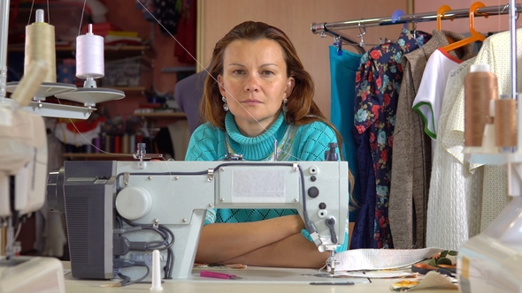 Seamstress Sits at the Workplace in Sewing Studio