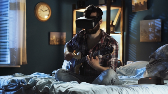 Man Playing Guitar in VR Glasses on Bed