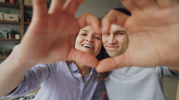 Portrait of Cheerful Multiethnic Couple Making Heart with Their Hands, Looking at Camera and Smiling