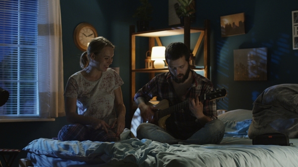 Playful Couple Singing with Guitar on Bed Late in Evening