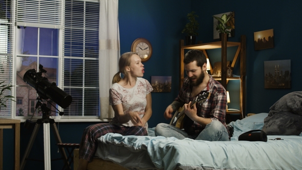 Playful Couple Singing with Guitar on Bed