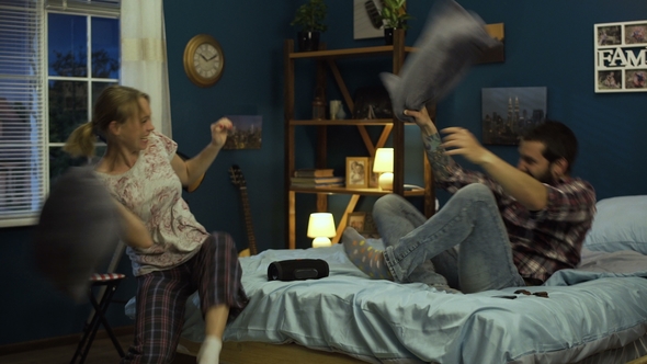 Laughing Couple Fighting with Pillows on Bed