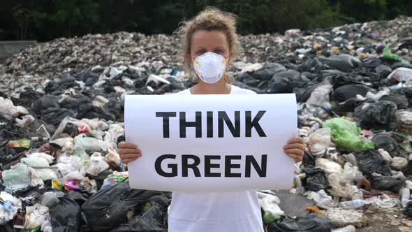 Young Woman Holding 'Think Green' Poster At Garbage Dump. Overconsumption.