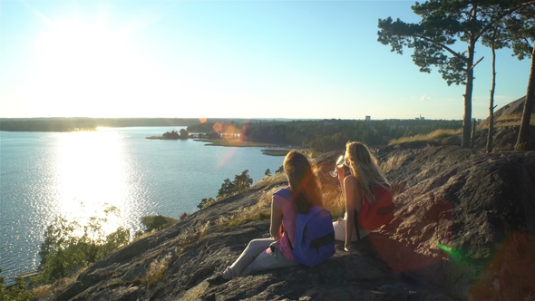 Female Couple Drinking Champagne on a High Rock in the Sunshine