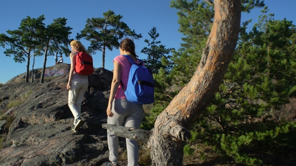 Two Active Young Women Help Each Other To Climb a High Rock