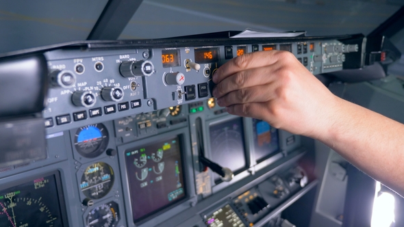 Multiple Buttons on a Plane's Console Are Being Pushed and Rotated By a Pilot