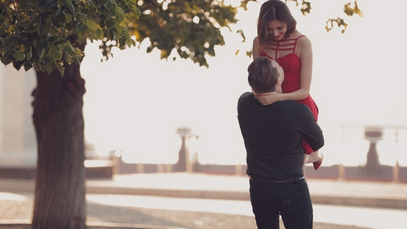 Young Guy Keeps His Favorite Girl. Loving Couple at Sunset