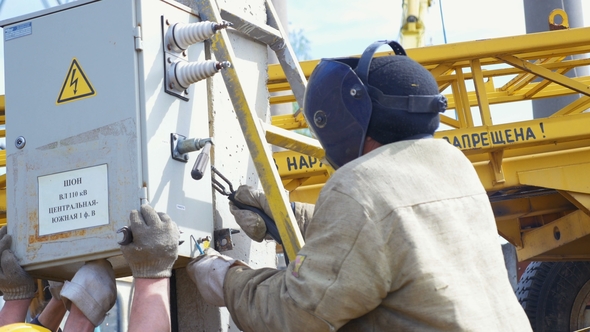 Person Holds Switchgear and Man Fixes Equipment Doing Welding alt