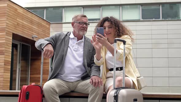 Beautiful Mature Couple with Suitcases is Sitting on a Bench Waiting for Their Flight