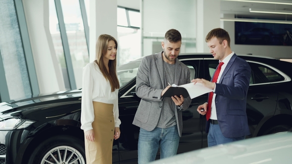 Young Bearded Man Is Buying Car for His Attractive Wife Signing Documents Shaking Hands with Manager