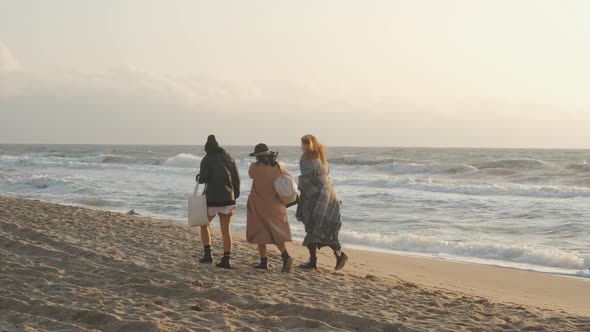 Three Beautiful Young Women Walking on the Sand Beach at Sunset or Sunrise