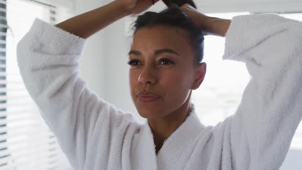 Mixed race woman standing in bathroom tying her hair