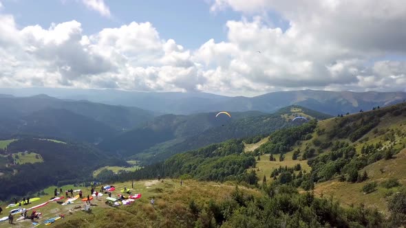 Aerial View of Paragliding Takeoff with Flying Paraglide Pilots in Mountains Landscape