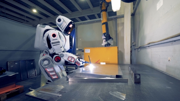 Factory Robot Is Working with Welding Equipment and a Metal Sheet at a Plant
