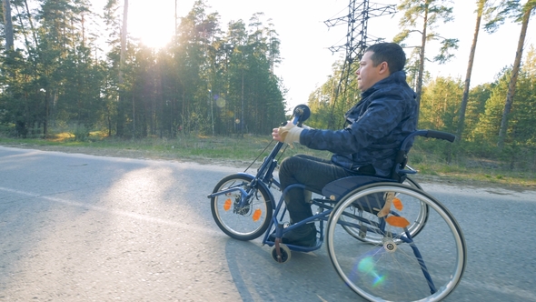 Handicapped Man Moving Along Road in a Training Wheelchair