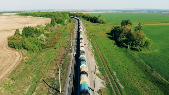 Freight Train with Tank Wagons Goes on a Long Railway Near Fields