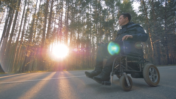 Physically Challenged Man Is Moving in a Powered Wheelchair Along the Road