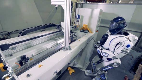 Industrial Robot Welder Standing Near Factory Machine with a Tablet Computer