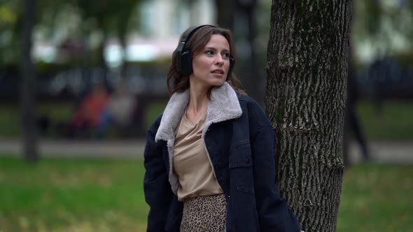 Inspired Young Woman Is Listening To Music By Wireless Headphones in Park, Enjoying Autumn Nature