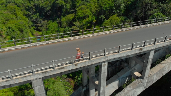 Aerial Shot of a Woman and Her Son Standing on a Tall Bridge Crossing a Canyon with a River on Its