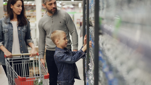 Adorable Child Is Taking Bottle of Water From Shelf in Supermarket and Putting It in Shopping Cart