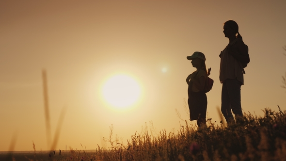 Mom and Daughter Are Admiring the Sunrise. They Stand with Backpacks Behind Their Backs in a
