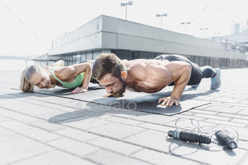 outdoor at city background. Couple doing hamstring leg exercise and stretches. Female amd male sports models exercising in summer at morning.