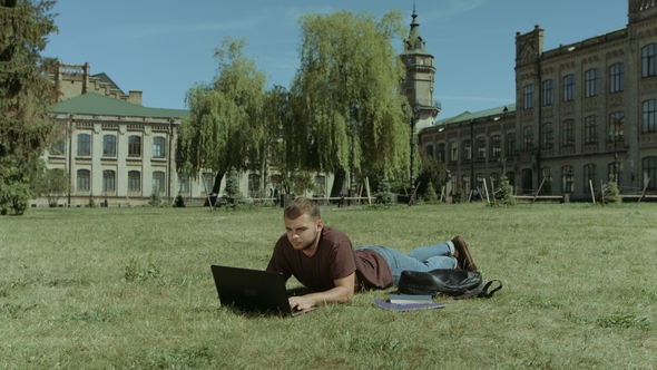 Smart Male Student Working on Laptop on Campus Lawn