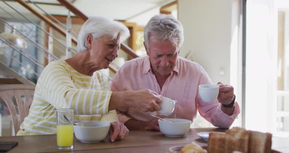 Senior caucasian couple pouring milk in cereal bowl having breakfast together at home