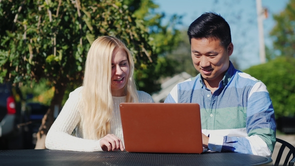 Young People Caucasian Woman and Chinese Man Are Using Laptop Together. Have a Rest on a Outdoors