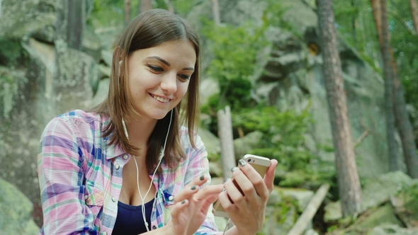 A Young Woman Tourist Uses a Smartphone in a Hike. Sits Resting Against the Rocks in the Mountains