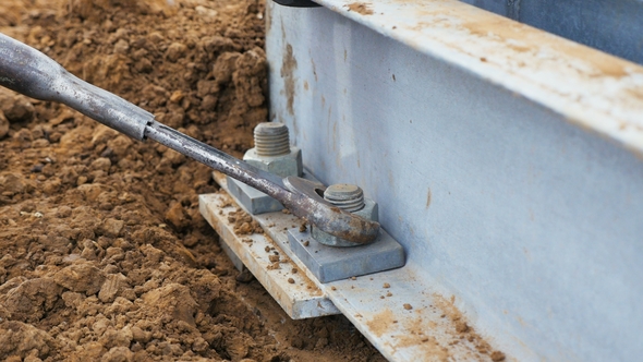 Worker Twists Screw on Metal Tower Support on Ground alt