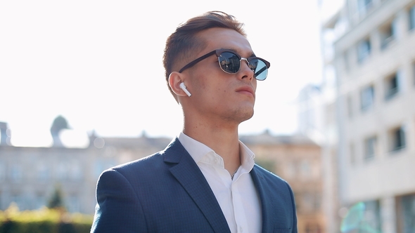 Young Businessman with Sunglasses Listening To the Music on His Smartphone Outdoors