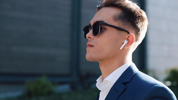 Young Businessman with Sunglasses Listening To the Music on His Smartphone Outdoors