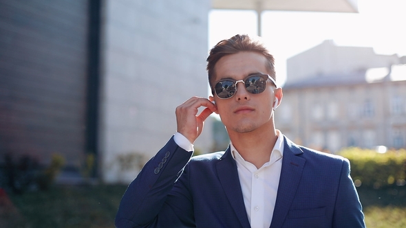 Happy Oung Businessman with Sunglasses Listening To the Music on His Smartphone Outdoors