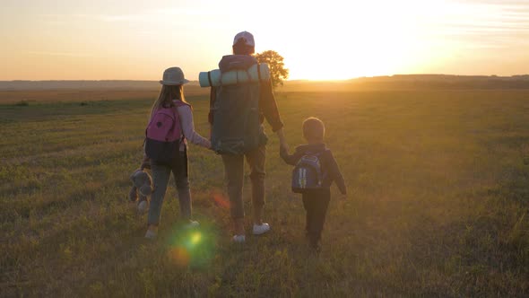 Mother and Two Children Walking in the Meadow at the Sunset Time. Silhouette Happy Beautiful Family