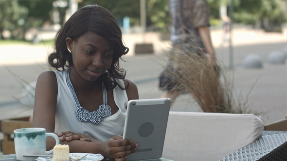 African American Woman Have Video Conferance on Her Tablet Sitting in Outside Cafe