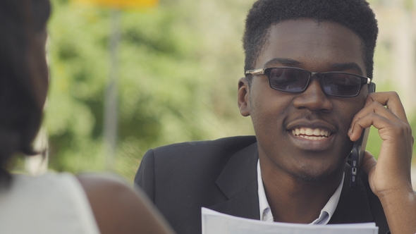 Young Positive Afro American Entrepreneur in Trendy Eyewear Having Phone Conversation with Secretary