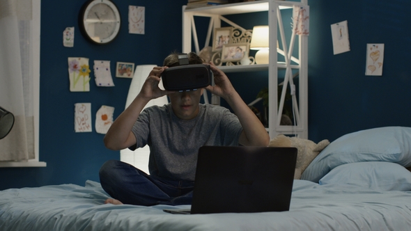 Boy Using VR Glasses and Laptop on Bed