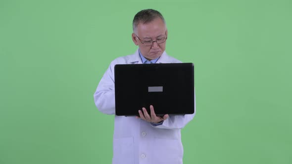 Happy Mature Japanese Man Doctor Thinking While Using Laptop