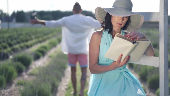 Curios Intelligent Elegant Woman Reading Book on the Right with Man Walking in Sunshine at