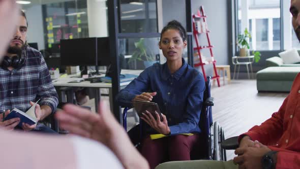 Mixed race businesswoman sitting in wheelchair discussing with diverse group of colleagues