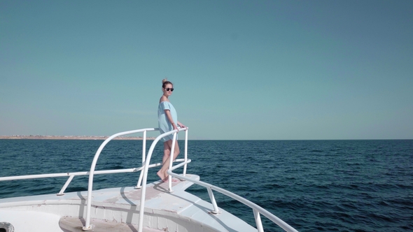Portrait of a Young Beautiful Sexy Caucasian Woman on a Yacht in in a Blue Dress and Sunglasses