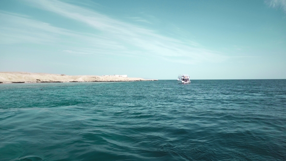 A Yacht in the Ocean with People on Board. Against the Background of a Rocky Desert Beach