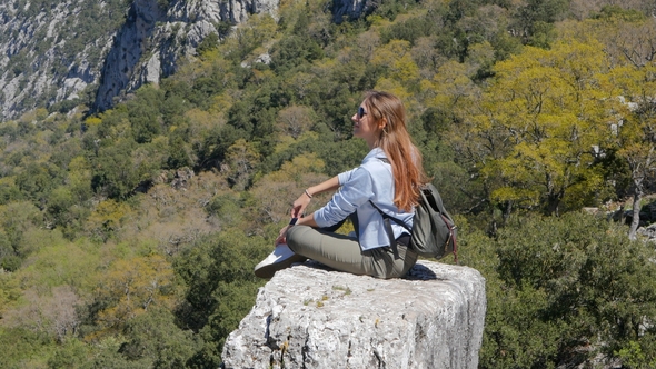 Young Woman Traveler Sits on the Rock
