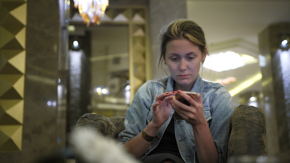 Young Caucasian Woman in a Jeans Jacket Uses a Smartphone, Writes Messages on the Social Network
